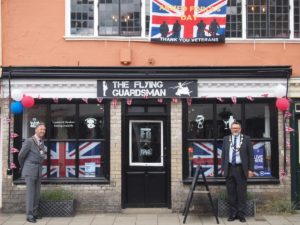 mayor of Hadleigh stands in front of a shop adorned with union jack flags for armed forces day window trail