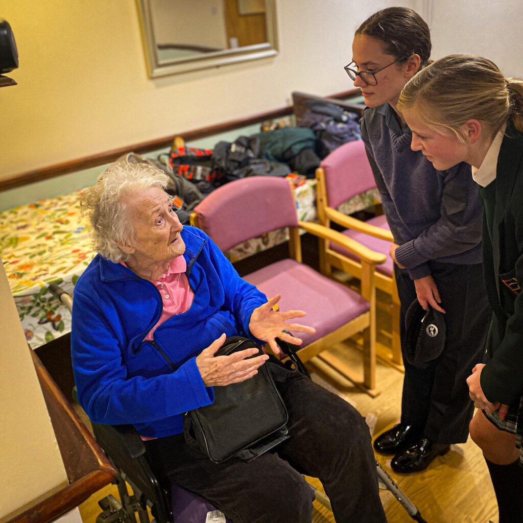 Two female air cadets listen as care home resident talks to them.