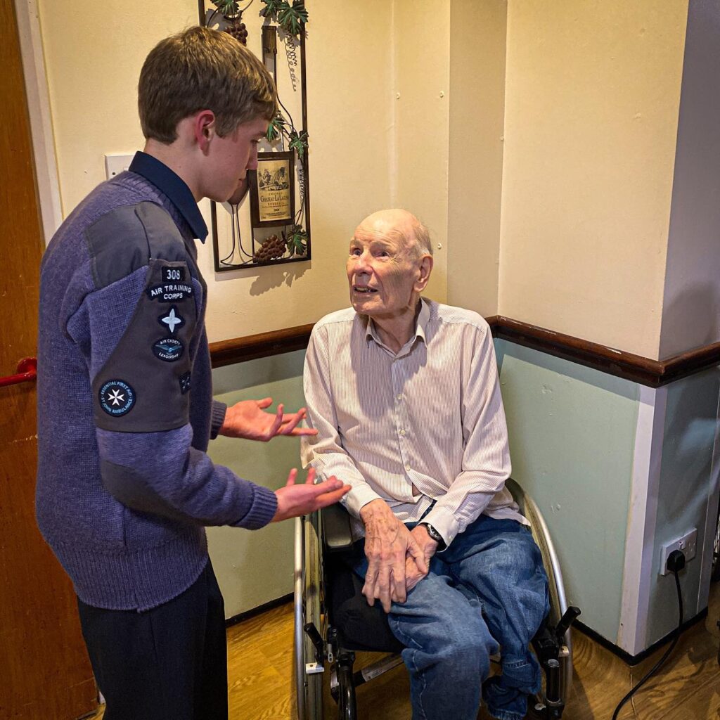 Male air cadet talks about his cadet experience with care home resident in a wheelchair.