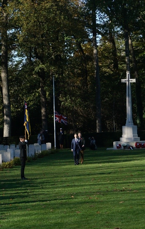 people in suits walking back across a cemetery after laying a wreath at the foot of a war memorial