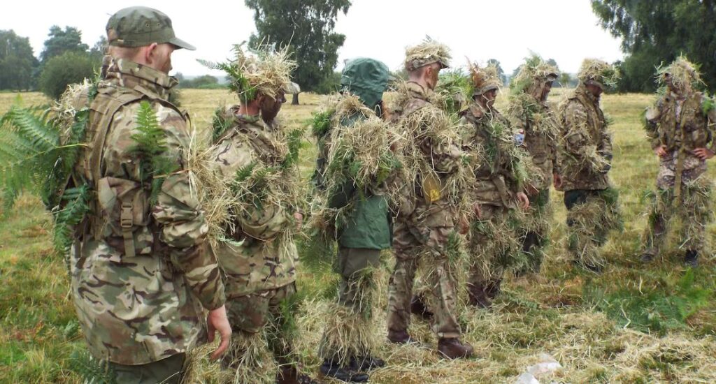 a group of cadets in full camouflage in a field with instructor