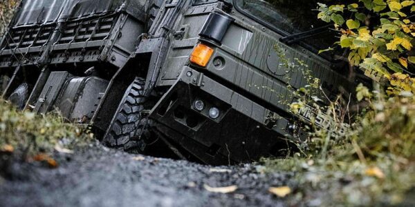 An Army vehicle driving over uneven woodland terrain