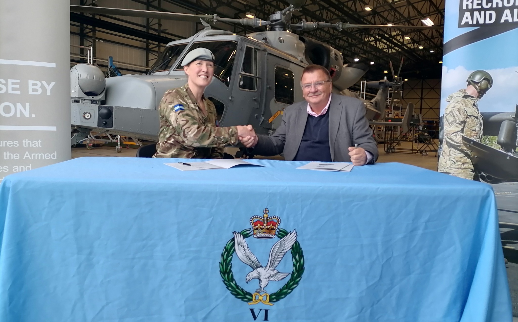 Lt Col Alice Archer and the representative for Armishaws Removals shake hands over the signed armed forces covenant pledge with an army helicopter in the background