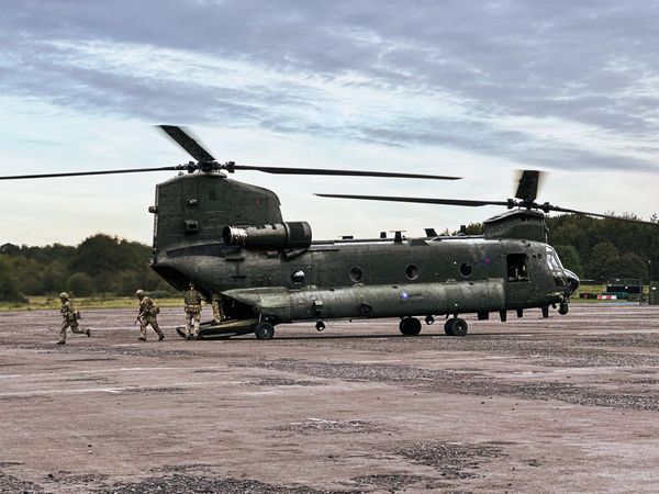 A large military transport helicopter on an airfield with reservists providing groundcrew support. 