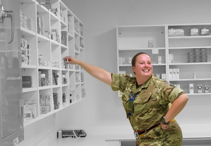 Reservist Jemma in uniform in a pharmacy smiling as she takes an item from the shelf